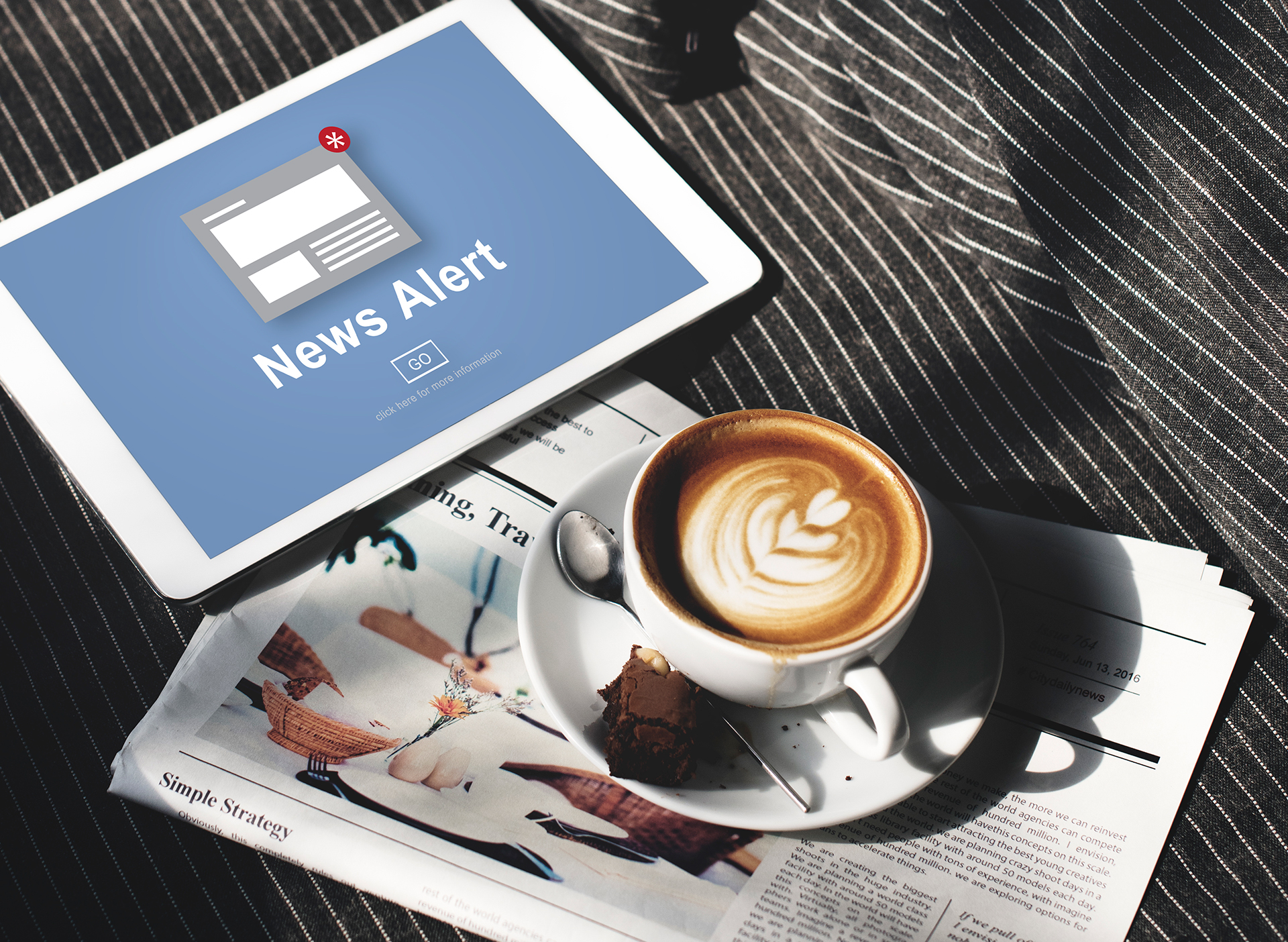 image of a news alert on a tablet screen with a latte and newspaper nearby