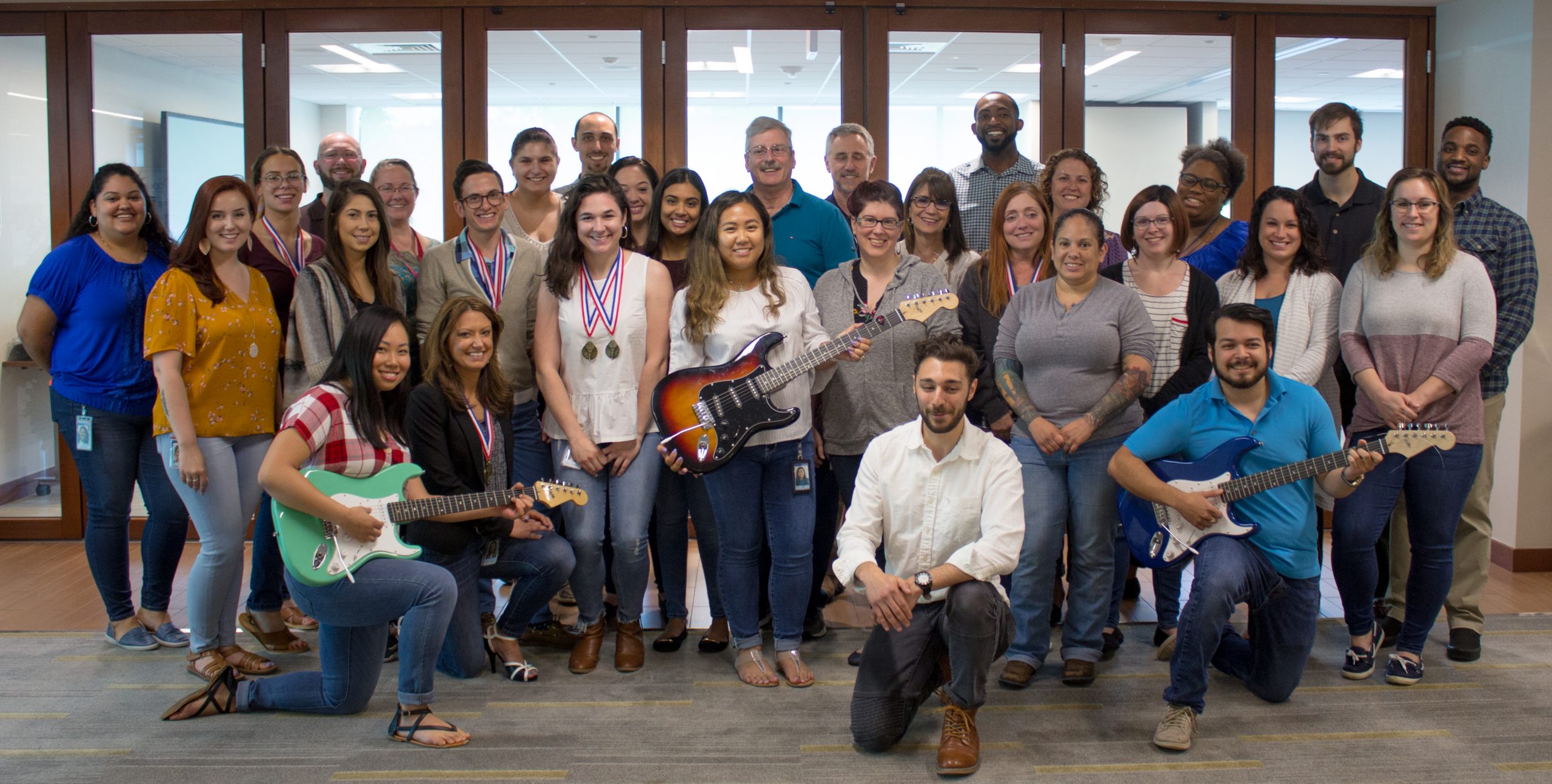 COCC Guitar Build Many COCC employees gathered in a group holding guitars assembled onsite